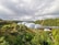 A lush landscape featuring large, geodesic dome structures surrounded by dense greenery and palm trees. Rolling hills covered in forests stretch across the background under an overcast sky.