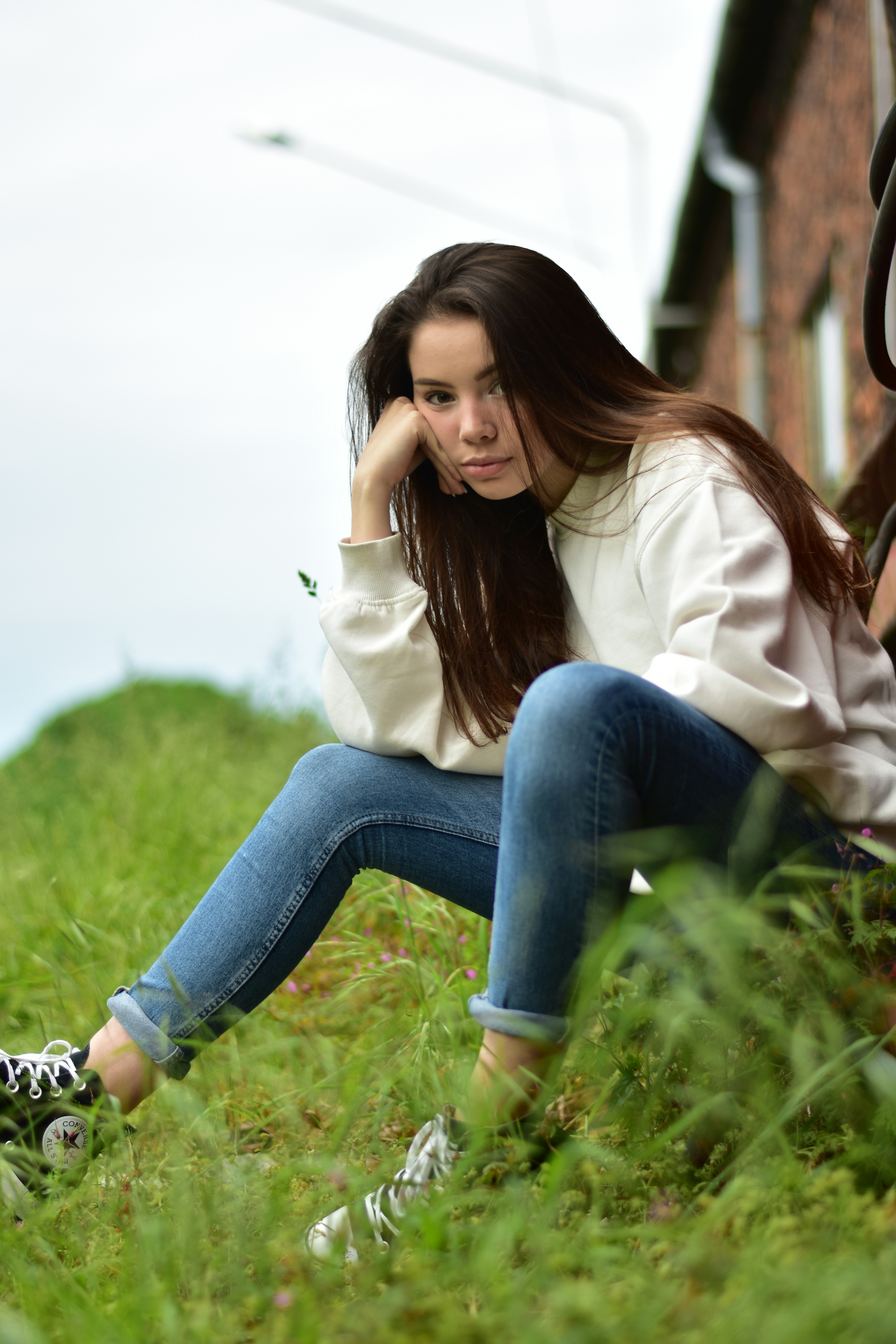 woman in white long sleeve shirt and blue denim jeans sitting on green grass during daytime