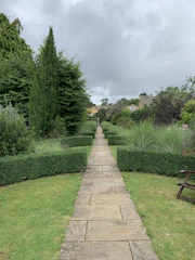 Stone pathway winding through a manicured garden with silver-gray gravel and green hedges.