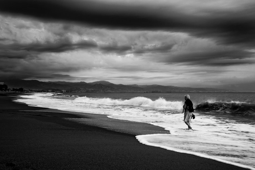 foto in scala di grigi di coppia che cammina sulla spiaggia