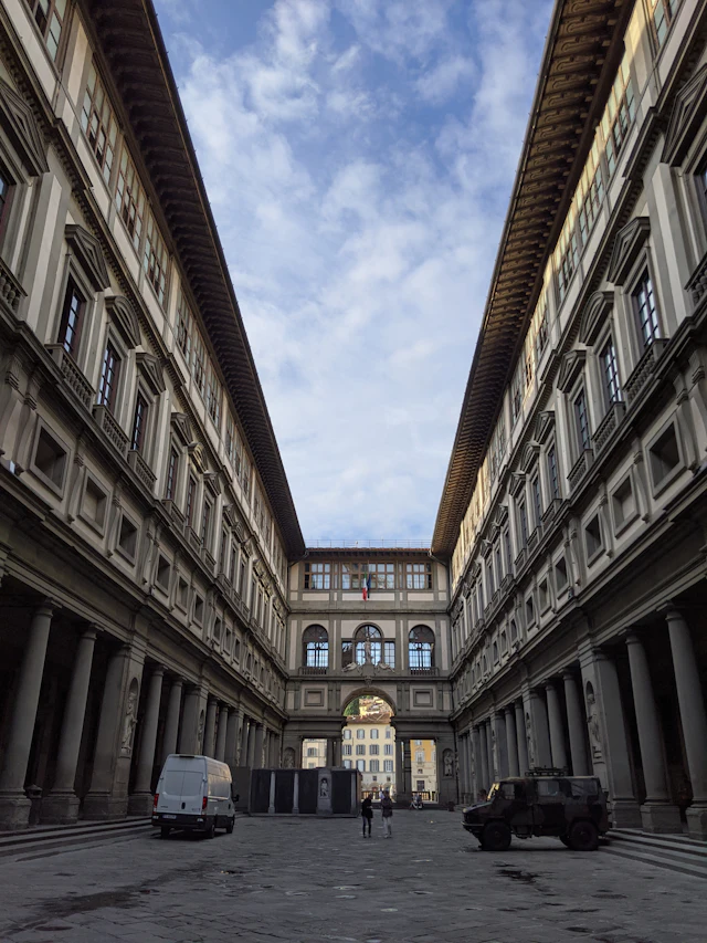 The Uffizi Gallery's U-shaped courtyard seen from ground level, its colonnaded wings framing a strip of sky toward the Arno.
