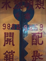 A large, vertical keyhole shape is painted against a yellow-orange background, with red and blue Chinese characters surrounding it. The numbers '9882' and '9259' are prominently displayed in bright red. The overall design has a vintage or traditional aesthetic.