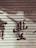 A metal roller shutter with peeling paint and faded red characters painted across it. The surface shows signs of wear and aging, giving a rustic appearance.
