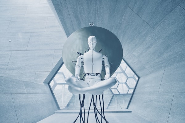 A white humanoid robot hovering in a grey, geometric concrete space with a sphere and cables behind them.