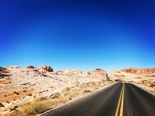 gray asphalt road between brown grass field during daytime in Valley of Fire State Park United States