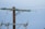 A wooden utility pole supports metal cross arms with glass insulators attached, holding up several taut power lines against a clear blue sky. The structure appears sturdy with electrical components visible at various points.
