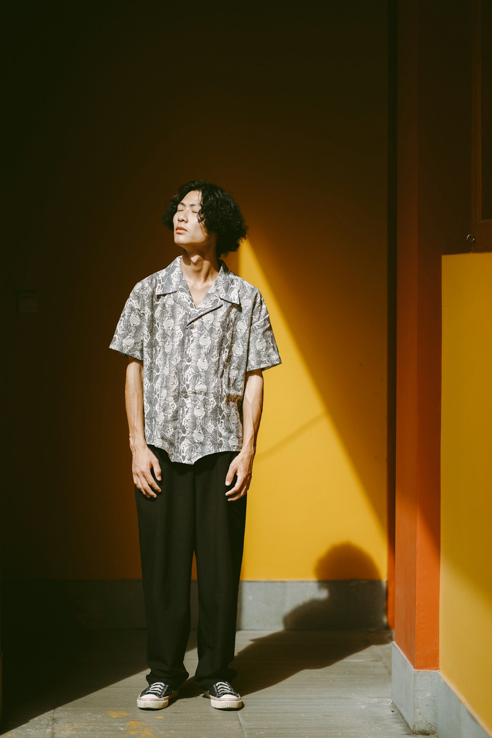 woman in white and black button up shirt and black pants standing beside yellow wall