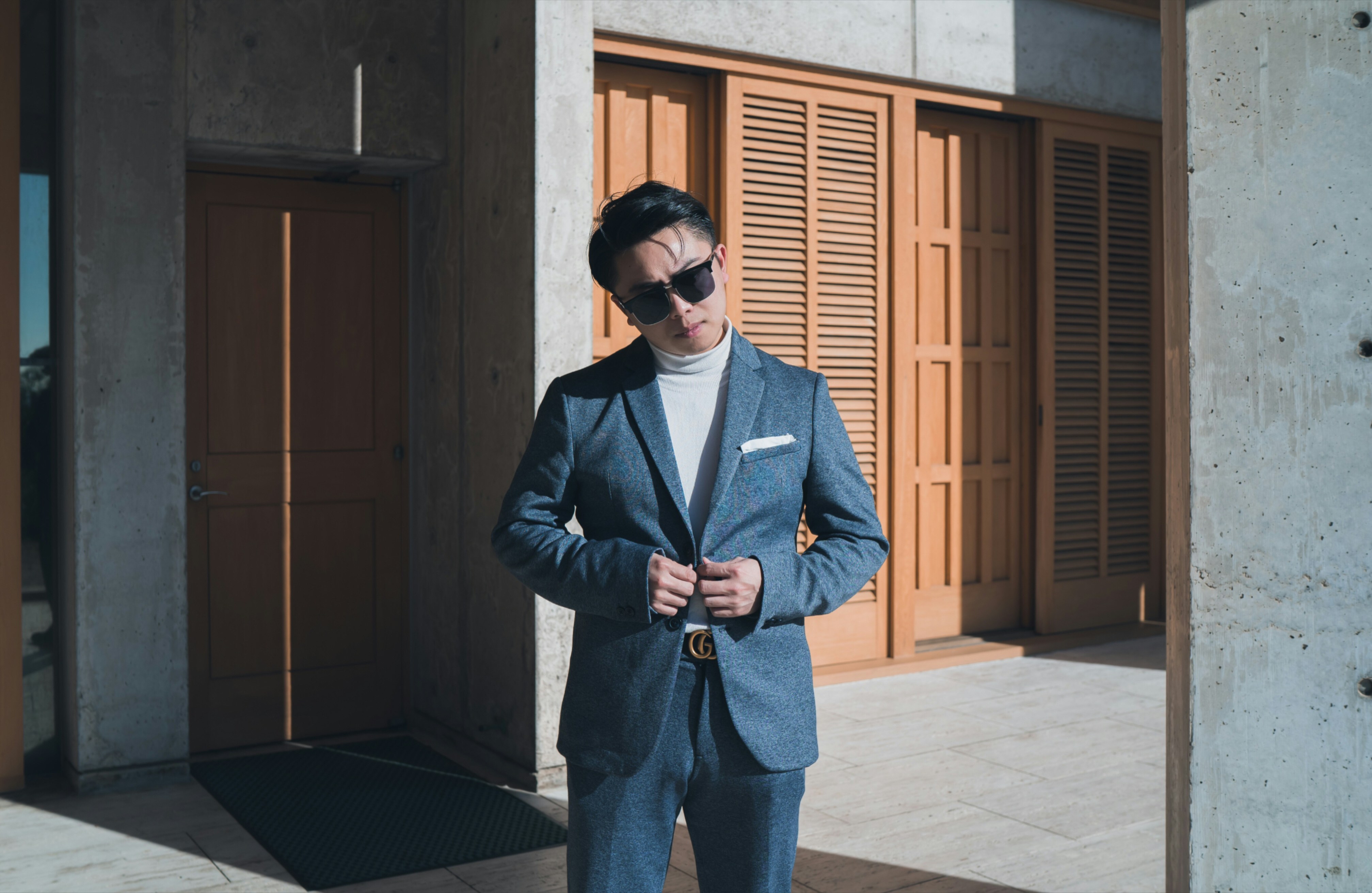 man in black suit jacket and blue denim jeans standing near brown wooden door