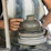 Close-up of a student shaping a clay pot on a spinning wheel in a sunlit studio.