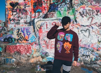 A candid shot of a young woman adjusting her stylish cap while leaning on a graffiti-covered wall.