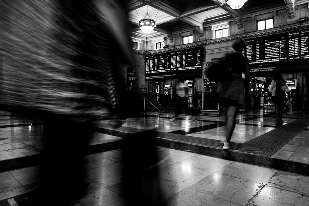 grayscale photo of woman walking on sidewalk