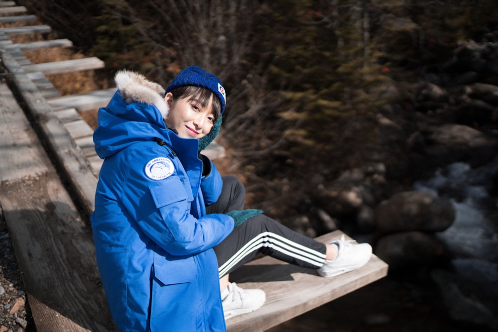 boy in blue jacket and blue knit cap sitting on brown wooden bench during daytime