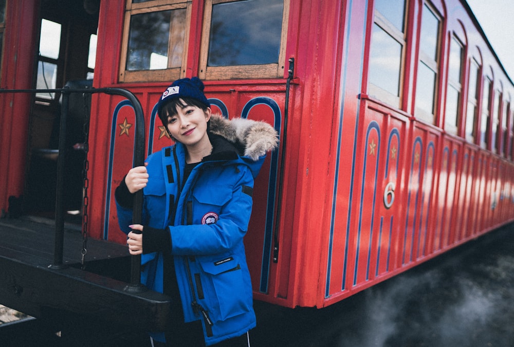 woman in blue parka coat standing beside red train