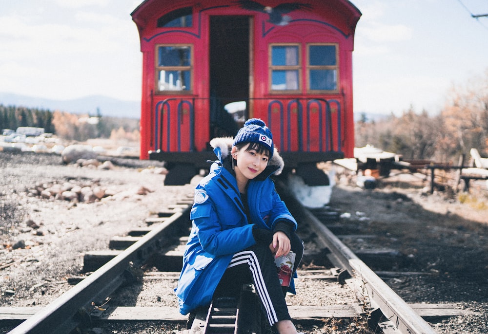 woman in blue jacket and blue knit cap sitting on train rail during daytime
