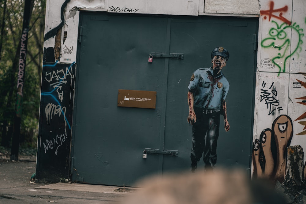 man in blue and black crew neck t-shirt and black pants standing beside green wall