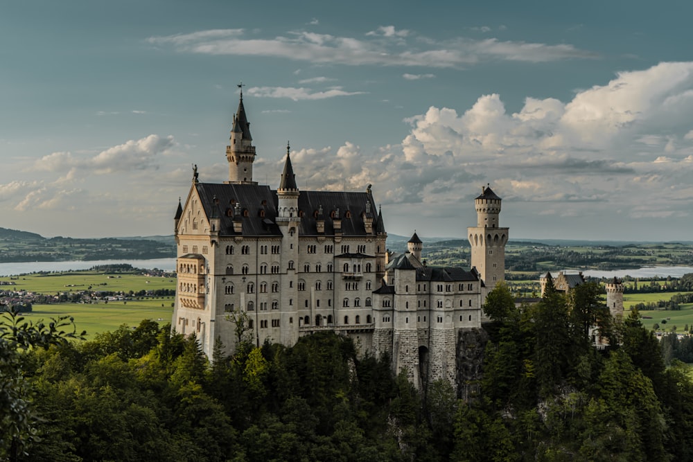 white and blue castle surrounded by green trees under blue and white cloudy sky during daytime