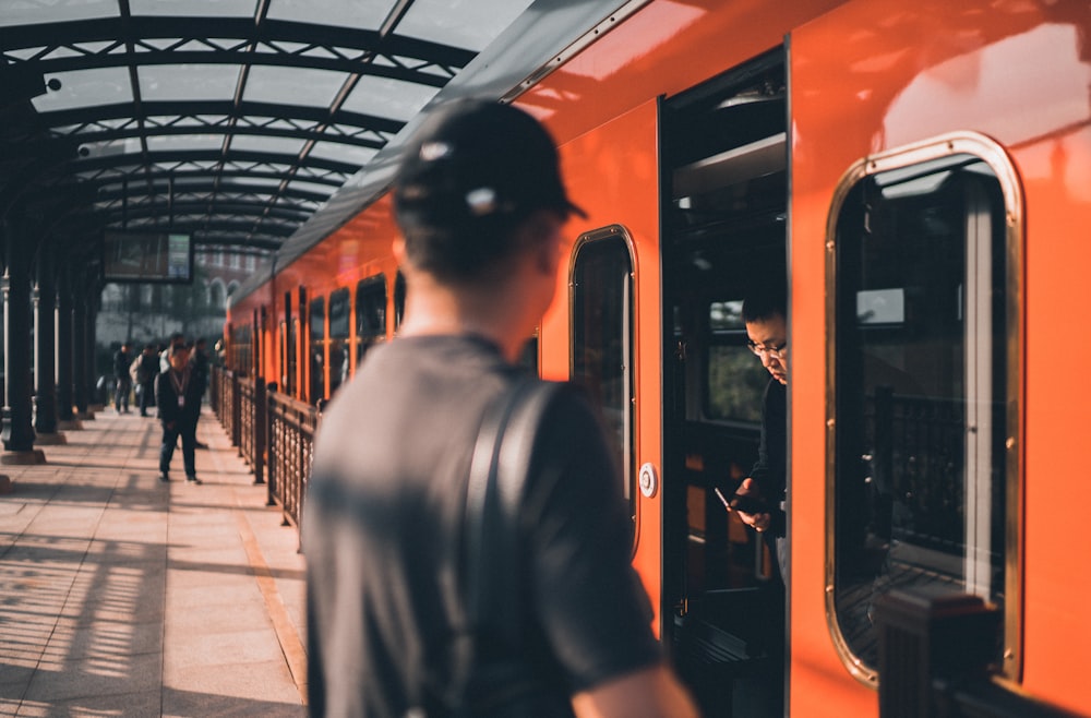 man in black leather jacket standing near orange train