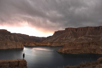 person standing on rock formation near lake under cloudy sky during daytime