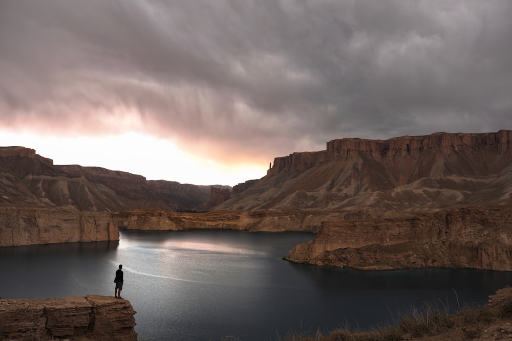 Persona parada en una formación rocosa cerca del lago bajo el cielo nublado durante el día