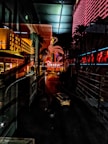 An urban night scene with illuminated buildings adorned with neon lights. A prominent neon flamingo sign and palm trees line the street, which is also occupied by a car. Reflections in the glass create an overlapping image effect, enhancing the vibrant atmosphere.