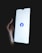 A hand holding a smartphone with a brightly lit screen displaying the Facebook logo in the center.