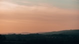 A serene landscape painting featuring rolling hills under a sunset.