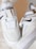 A pair of white sneakers featuring a sleek design with black swoosh logos. They have a modern, strap-based closure system and perforations on the toe area for breathability.