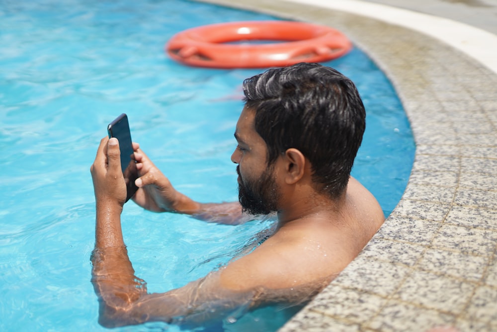 man in swimming pool holding smartphone