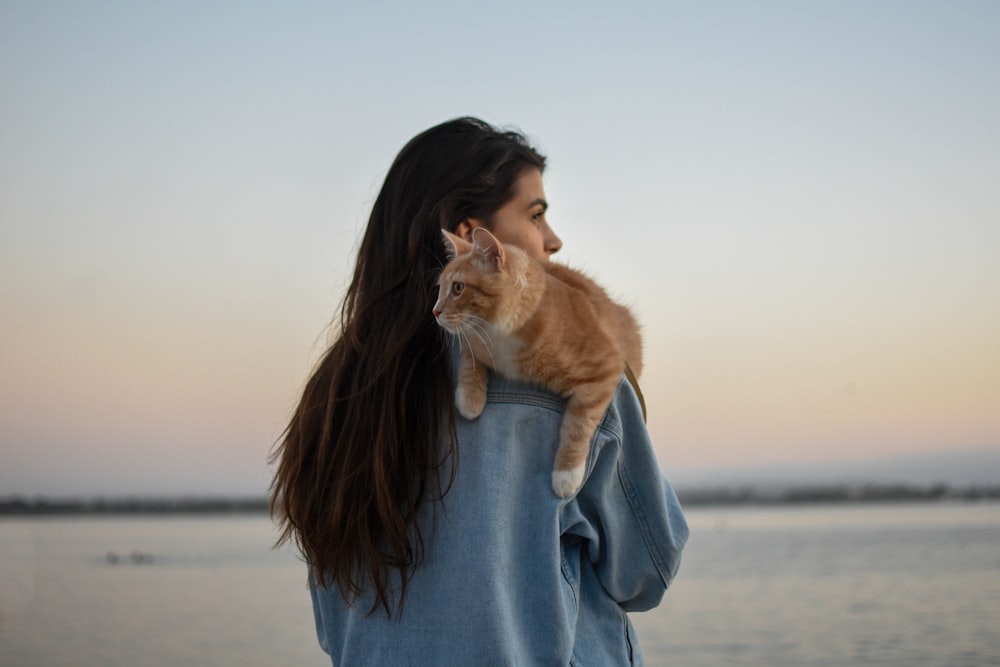 woman in gray sweater holding orange tabby cat
