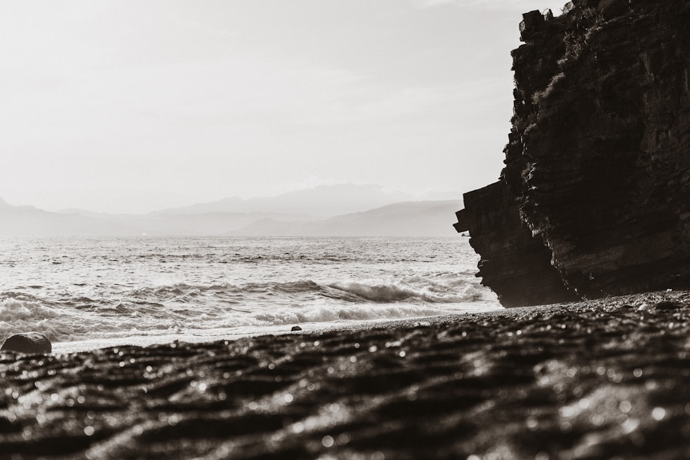 grayscale photo of rocky mountain by the sea
