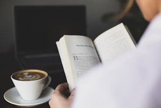 A close-up of a hand holding a book with a cup of coffee.