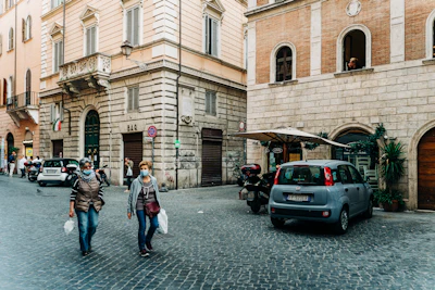woman in white jacket walking on sidewalk near cars parked beside brown building during daytime
