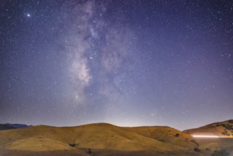 Rolling hills under a vast, star-studded night sky with the Milky Way visible