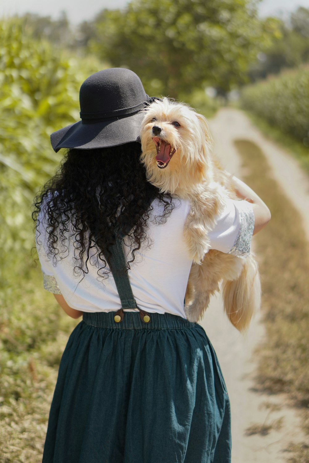Frau mit schwarzem Hut trägt braunen, langhaarigen kleinen Hund