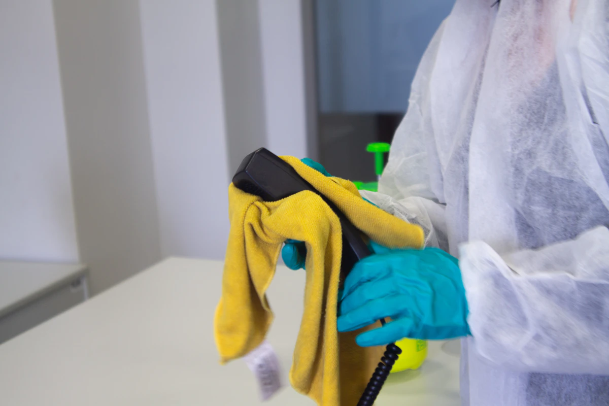 Reinigungskraft in Schutzkleidung mit gelbem Mikrofasertuch und Sprühflasche