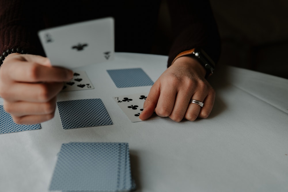 Person mit Spielkarten auf weißem Tisch
