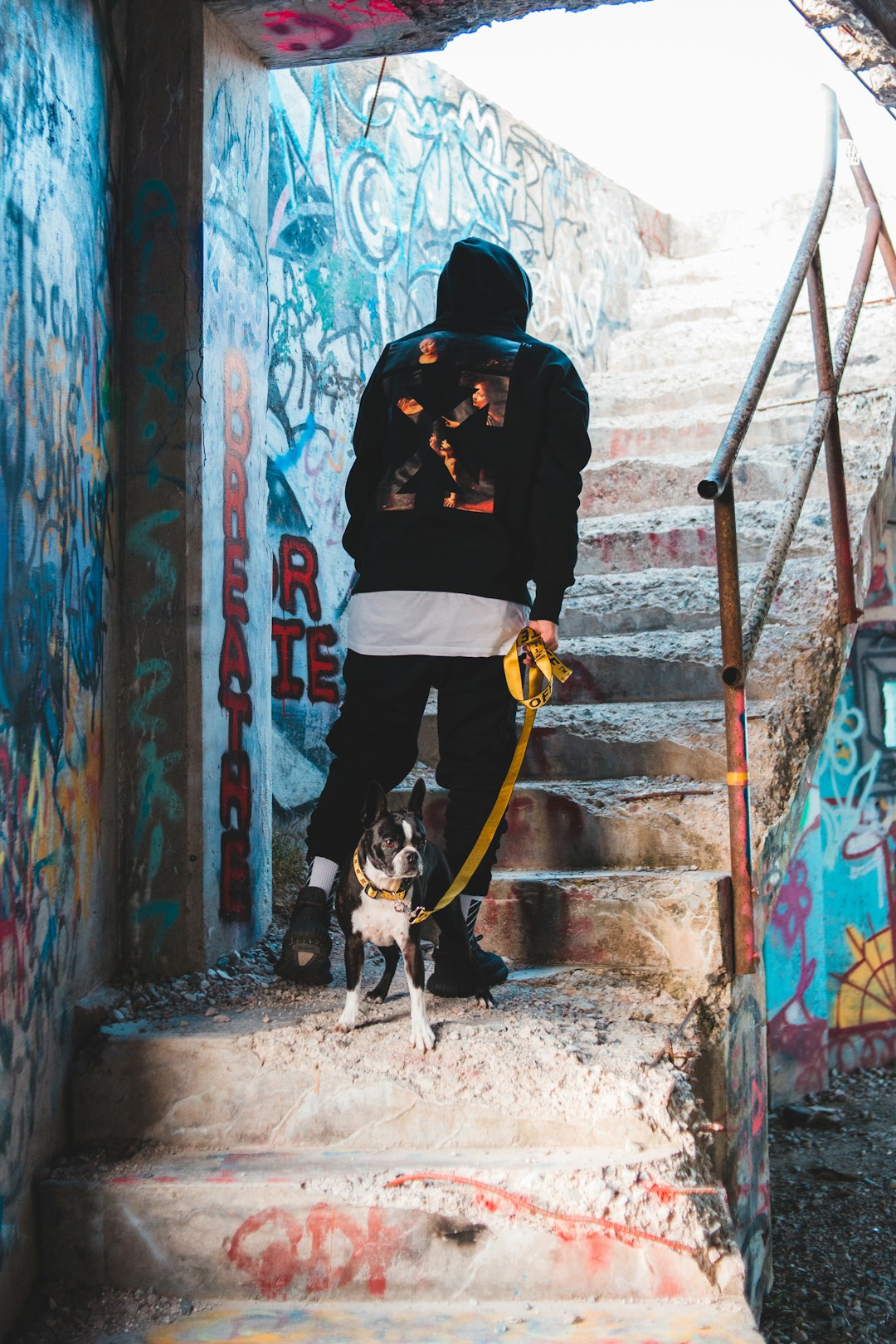 man in black hoodie and yellow pants holding black and white short coated medium sized dog