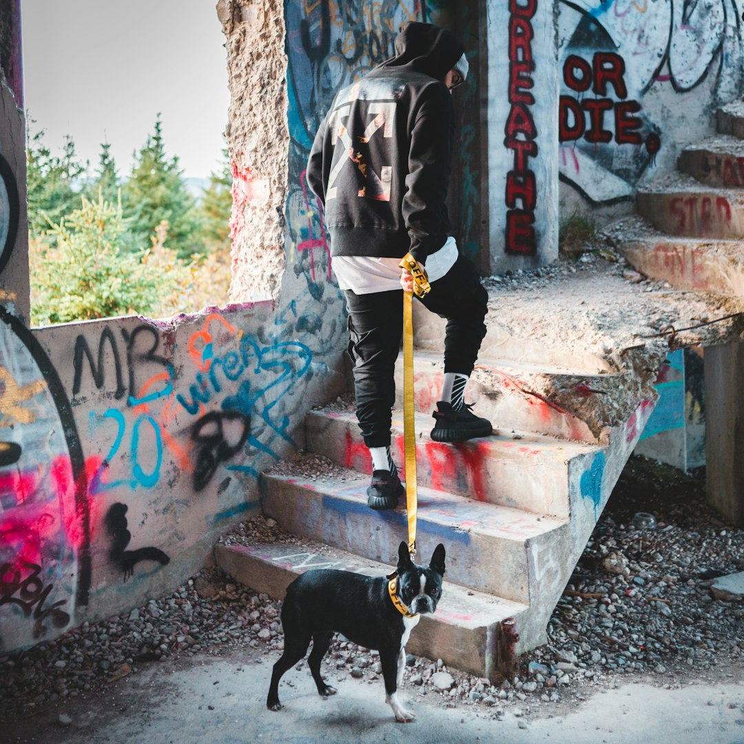 man in black jacket and black pants standing beside black short coated dog