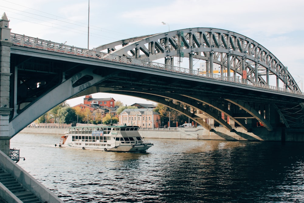 white and black boat on body of water under bridge during daytime