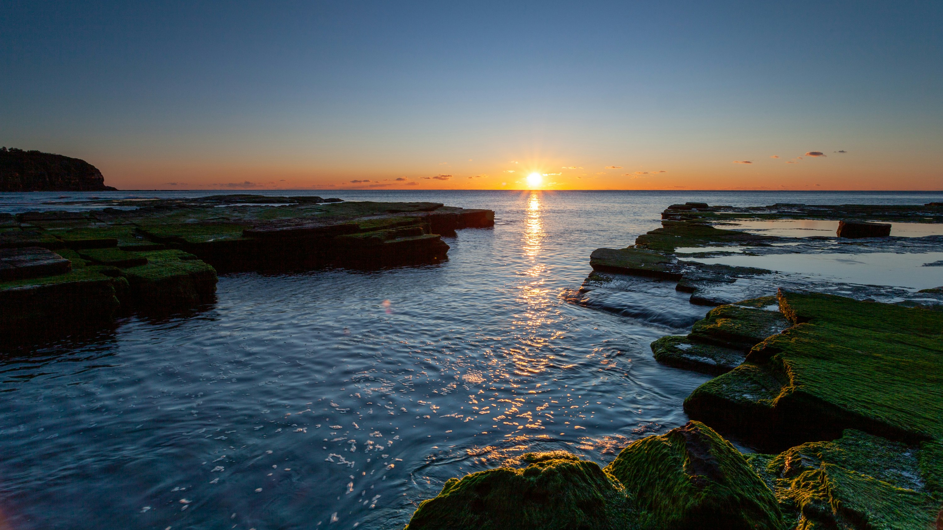 green moss on rock formation on body of water during sunset