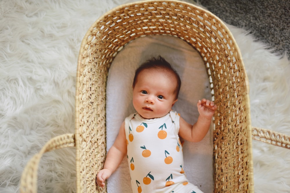 茶色の籐のバスケットに横たわっている白と緑の水玉模様のワンジーの赤ちゃん