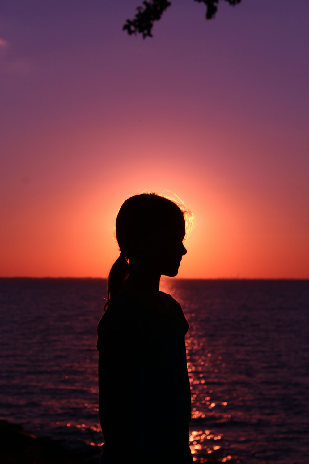 silhouette of woman standing near body of water during sunset