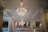 An elegant interior with large, ornate chandeliers hanging from a decorative ceiling. The chandeliers are intricately designed with multiple tiers of crystals. The walls feature patterned panels, and there are balconies overlooking the main area.