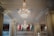 An elegant interior with large, ornate chandeliers hanging from a decorative ceiling. The chandeliers are intricately designed with multiple tiers of crystals. The walls feature patterned panels, and there are balconies overlooking the main area.