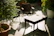 A sunlit patio featuring a stylish outdoor loveseat with plush cushions surrounded by greenery.