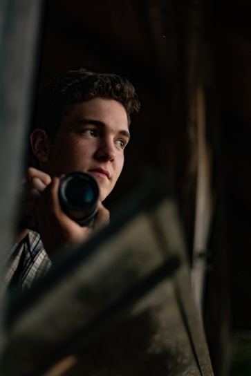 A candid portrait of a photographer holding a camera, standing in a softly lit urban setting.