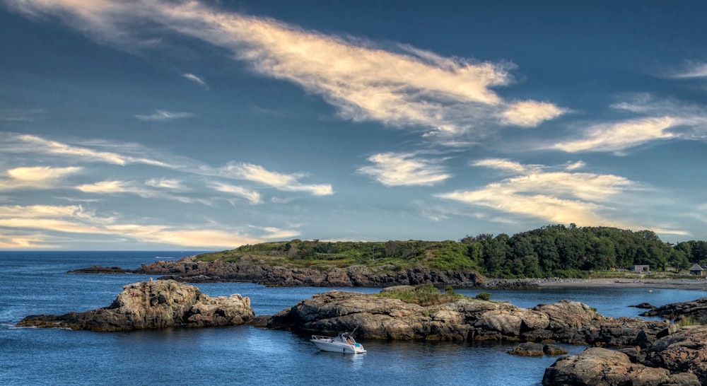 green trees and brown rocks on blue sea under blue and white cloudy sky during daytime