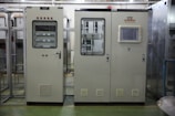 Industrial control panels with various buttons, switches, and display screens are placed in a well-lit environment. The setup suggests a technical or engineering setting with panels housing electronic or communication equipment.