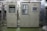Industrial control panels with various buttons, switches, and display screens are placed in a well-lit environment. The setup suggests a technical or engineering setting with panels housing electronic or communication equipment.