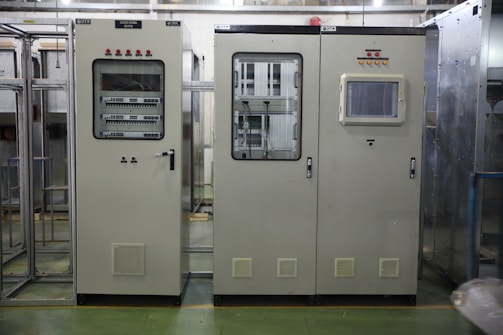 Industrial control panels with various buttons, switches, and display screens are placed in a well-lit environment. The setup suggests a technical or engineering setting with panels housing electronic or communication equipment.